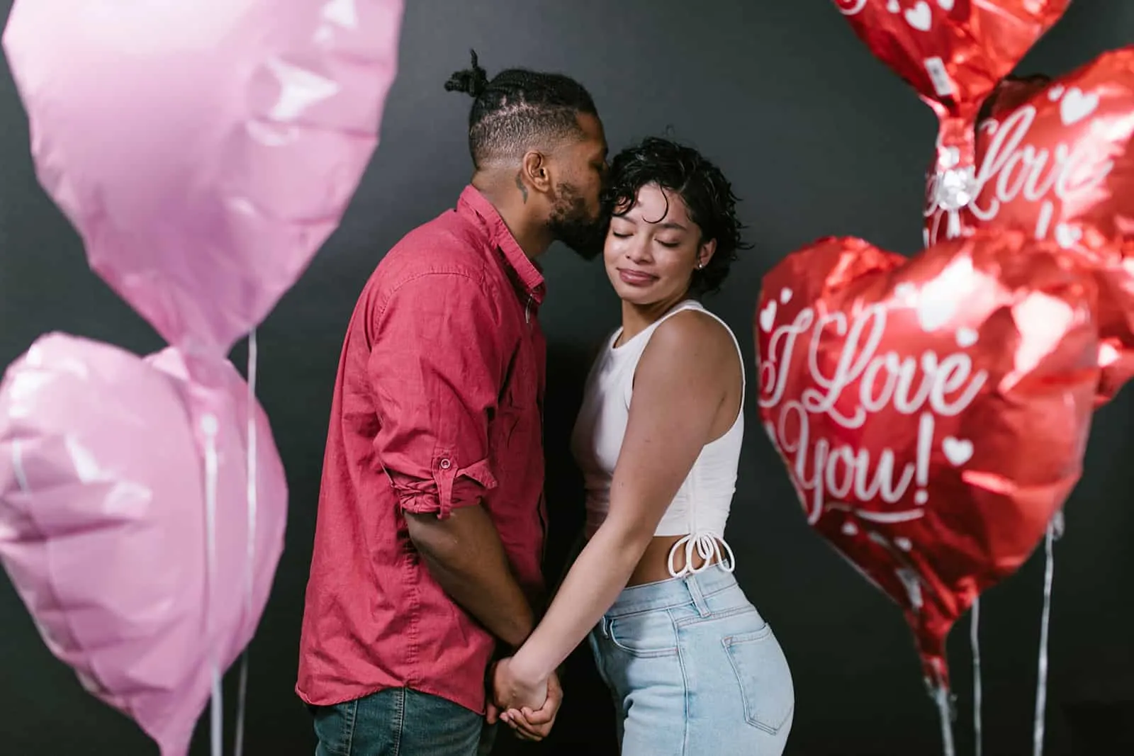 man kissing his girlfriend on a cheek while standing together between balloons