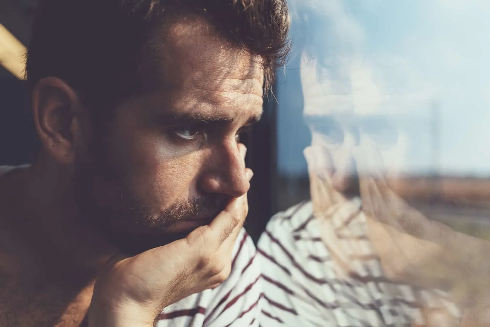 sad man in striped shirt looking through window