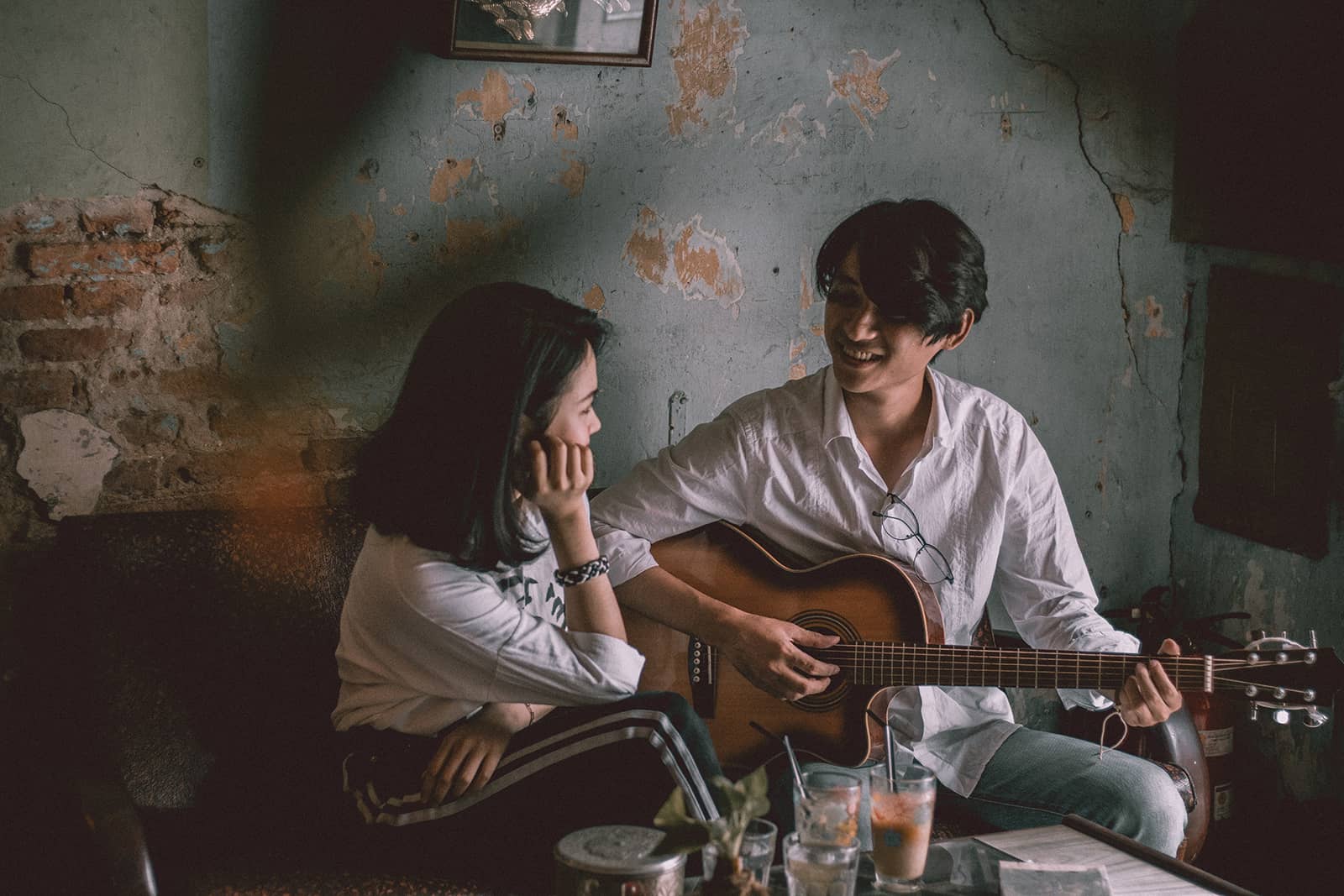 man playing guitar to a smiling woman while sitting together on the couch