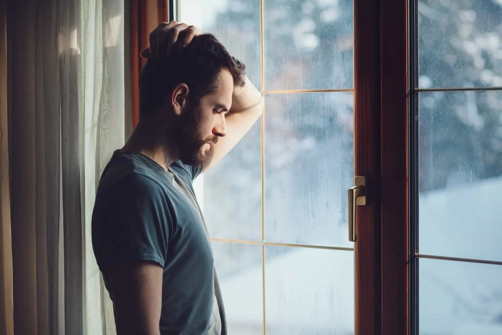 sad man standing near window during daytime
