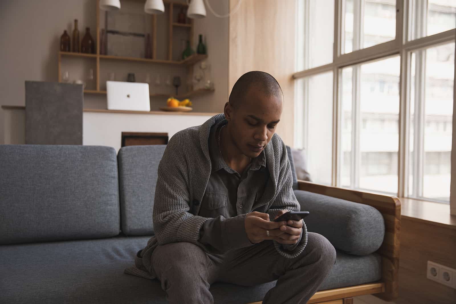 uomo che scrive sul suo smartphone seduto sul divano di casa