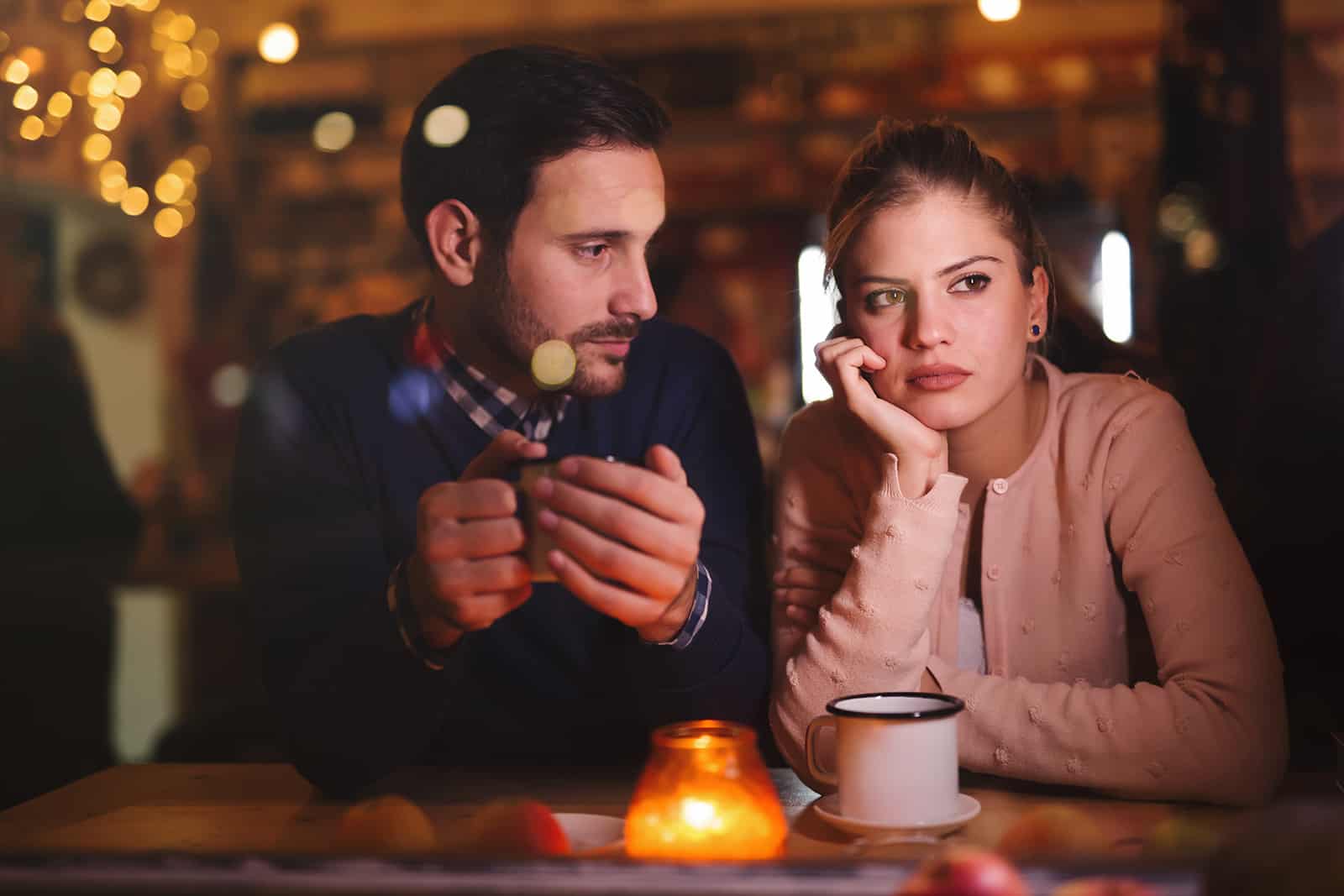 donna pensierosa seduta con il suo fidanzato in un caffè e con lo sguardo rivolto altrove