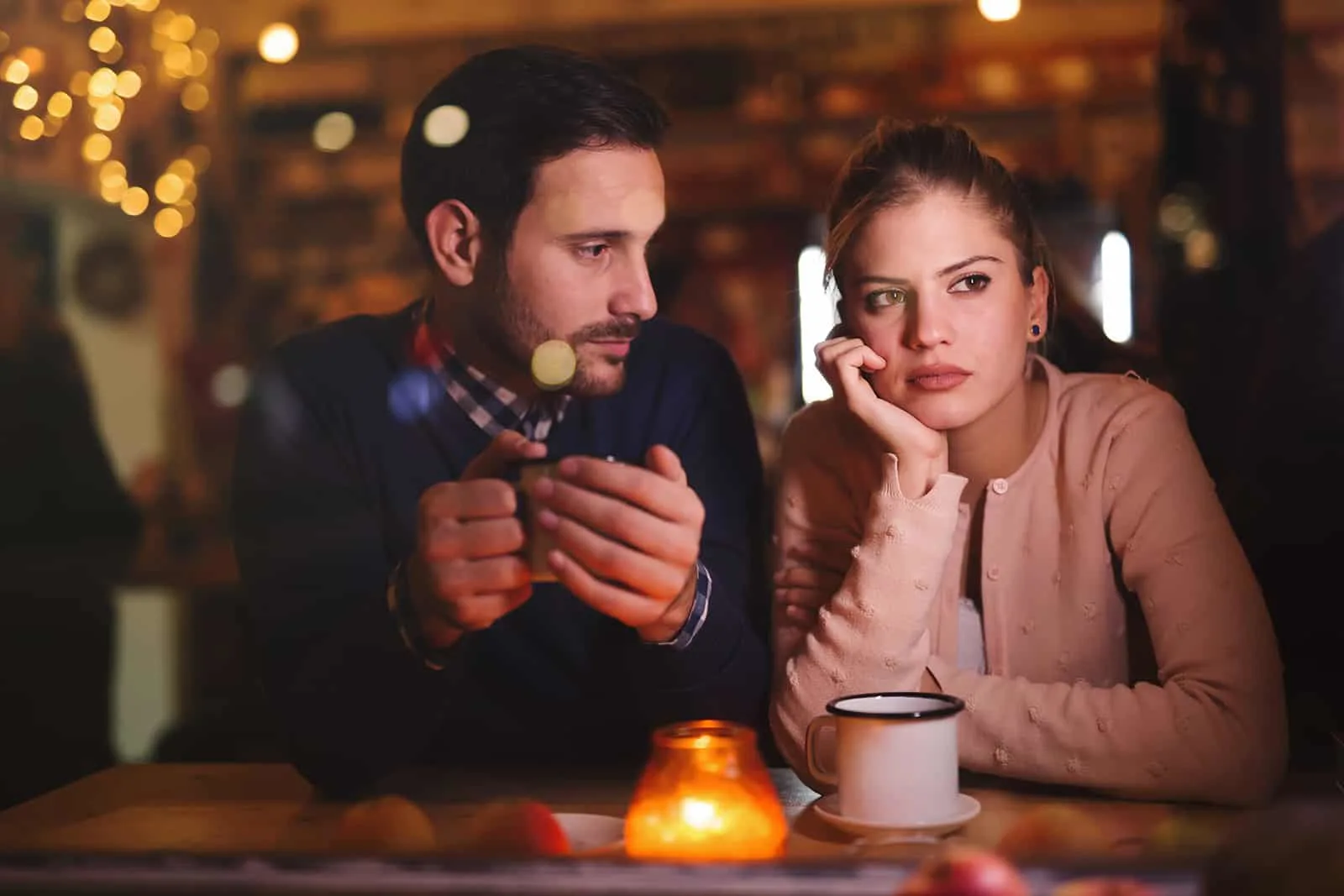 pensive woman sitting with her boyfriend in a cafe and looking aside