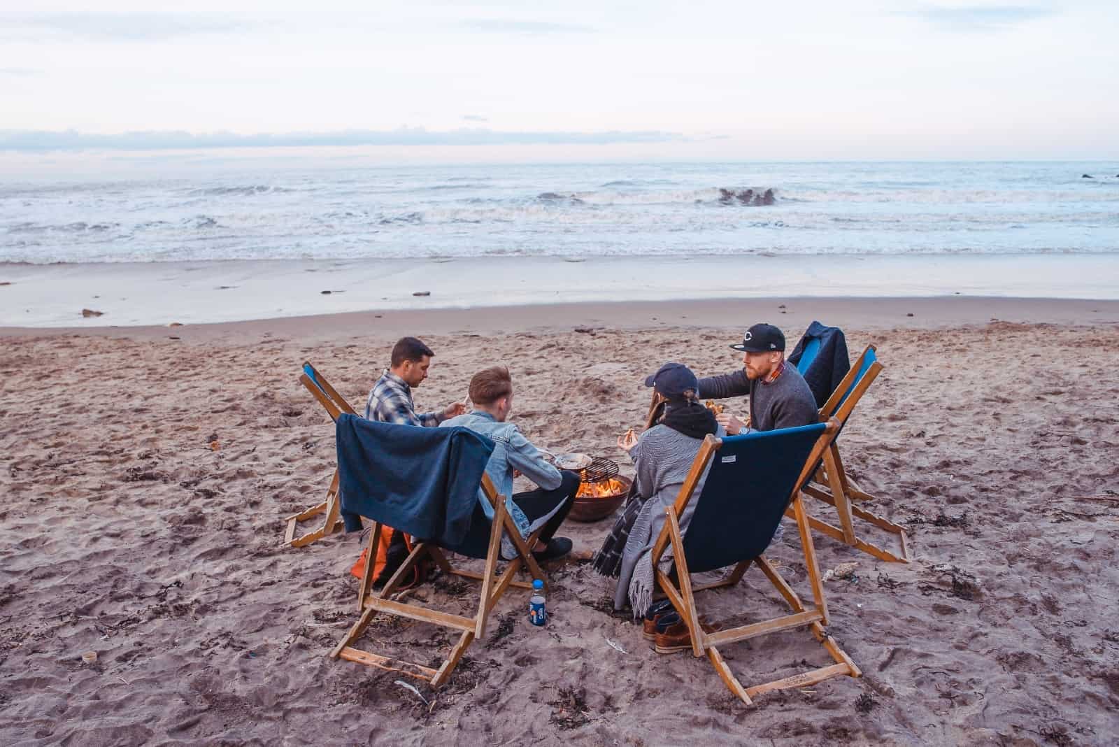 cuatro personas sentadas en la playa cerca de una hoguera