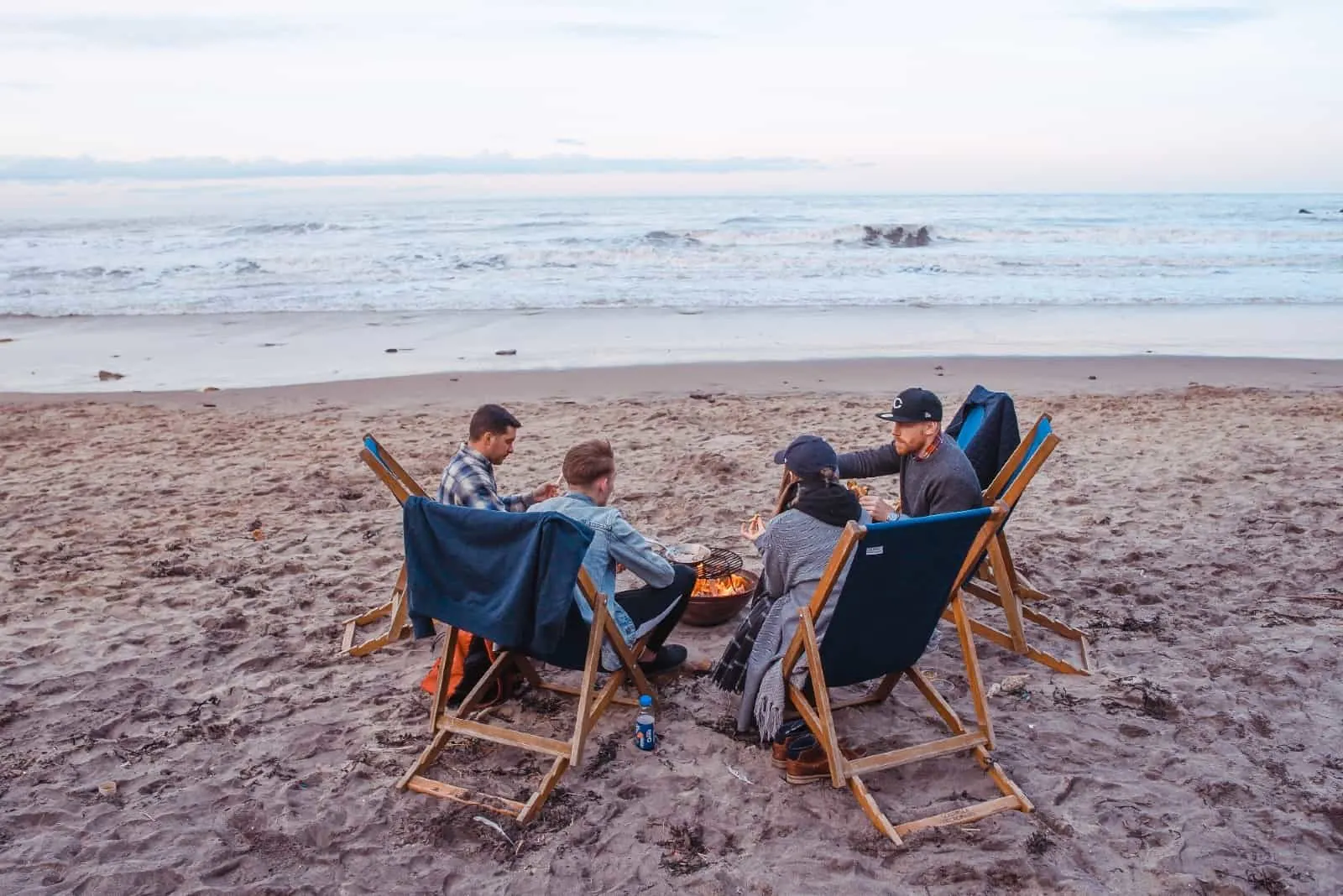 four people sitting on beach near fire pit