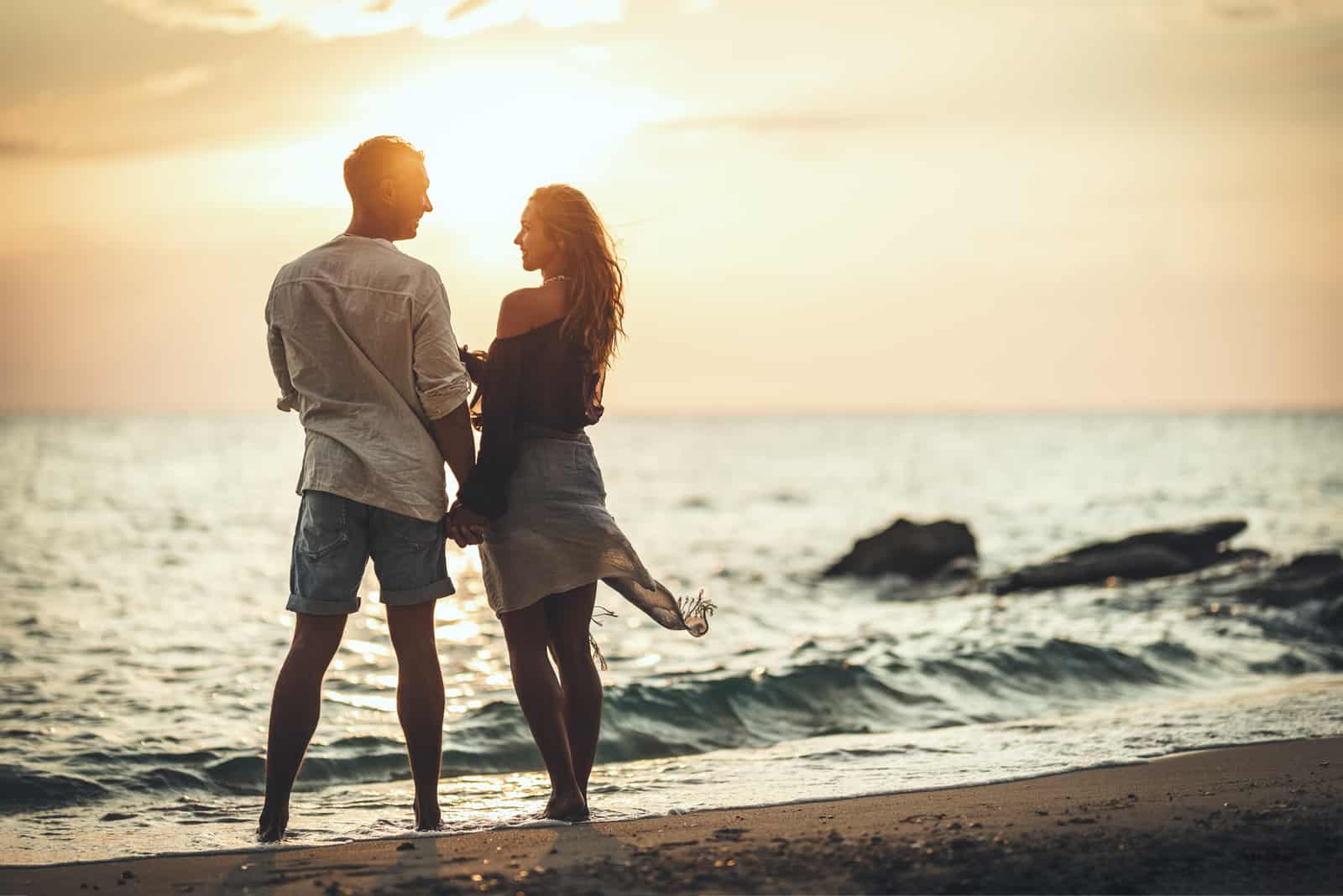 casal romântico ao pôr do sol na praia a conversar