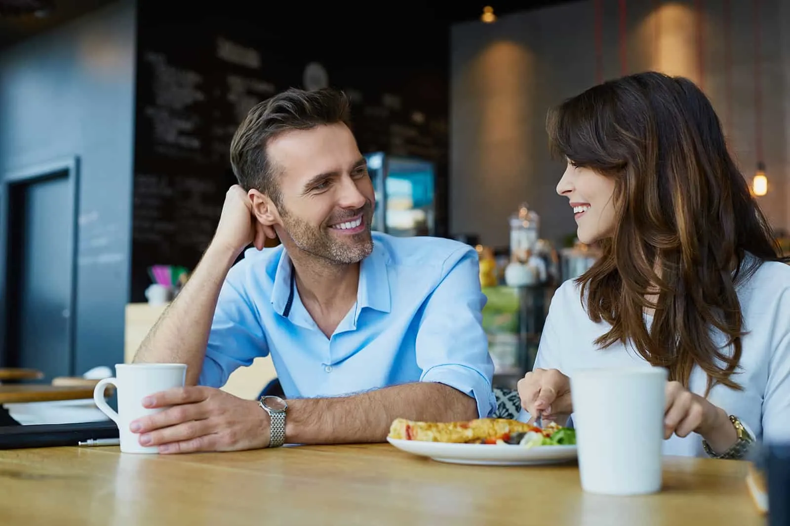 smiling man looking at a woman while having lunch in a cafe