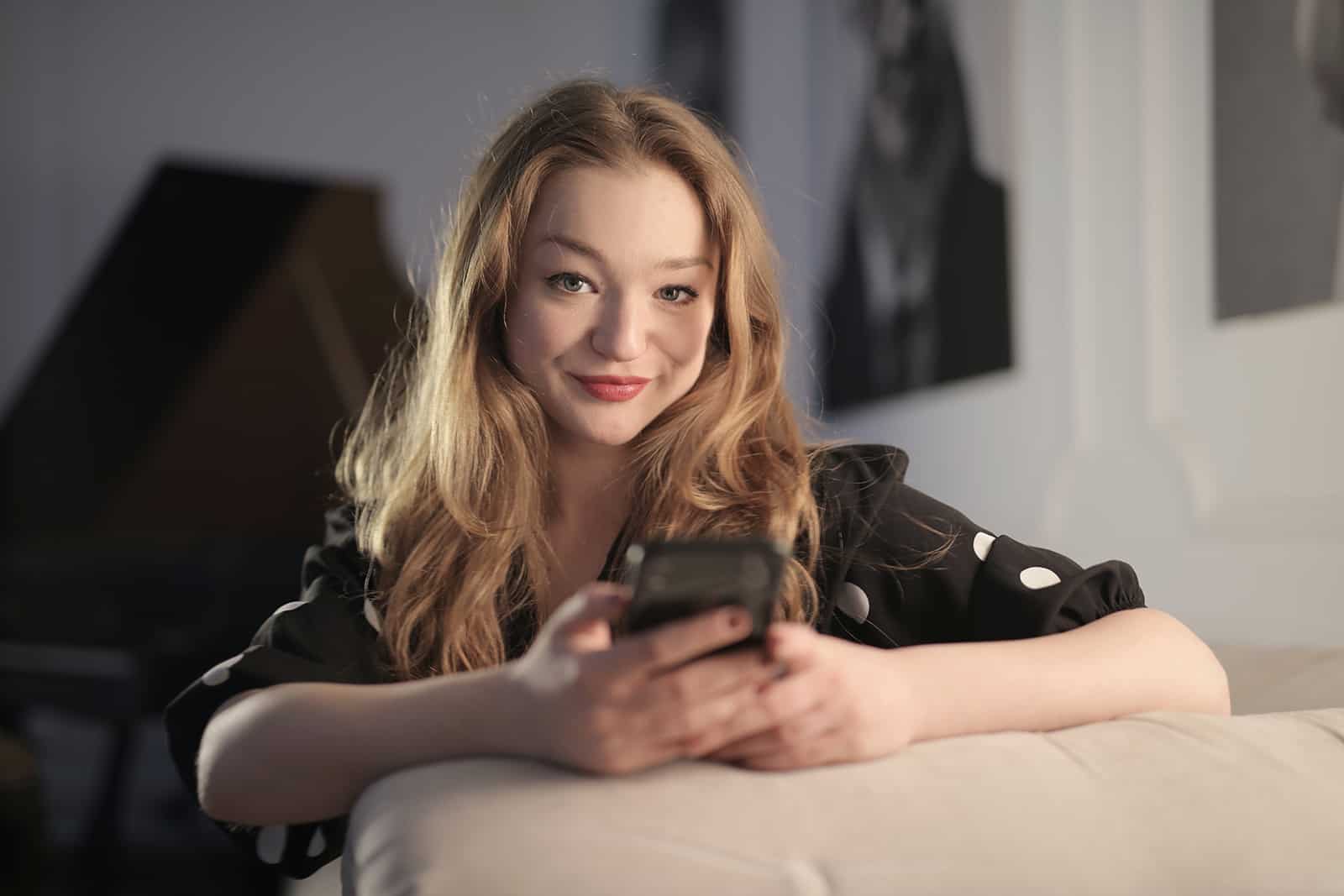smiling woman holding smartphone while sitting on the couch