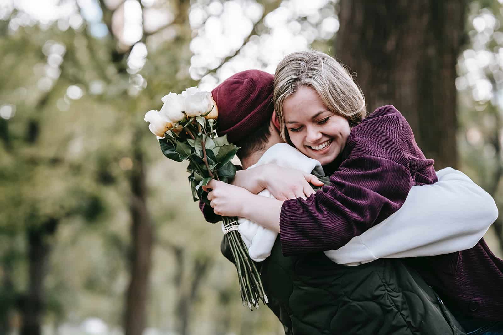 smiling woman hugging her boyfriend while holding white roses