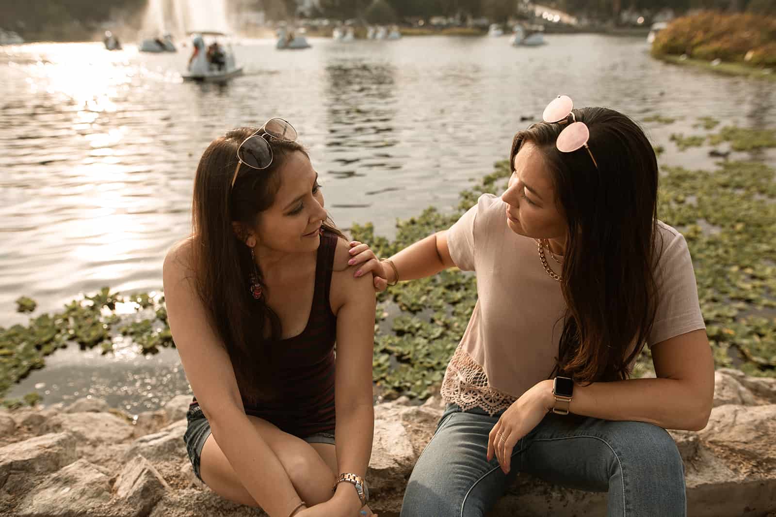 two female friends talking while sitting near the lake