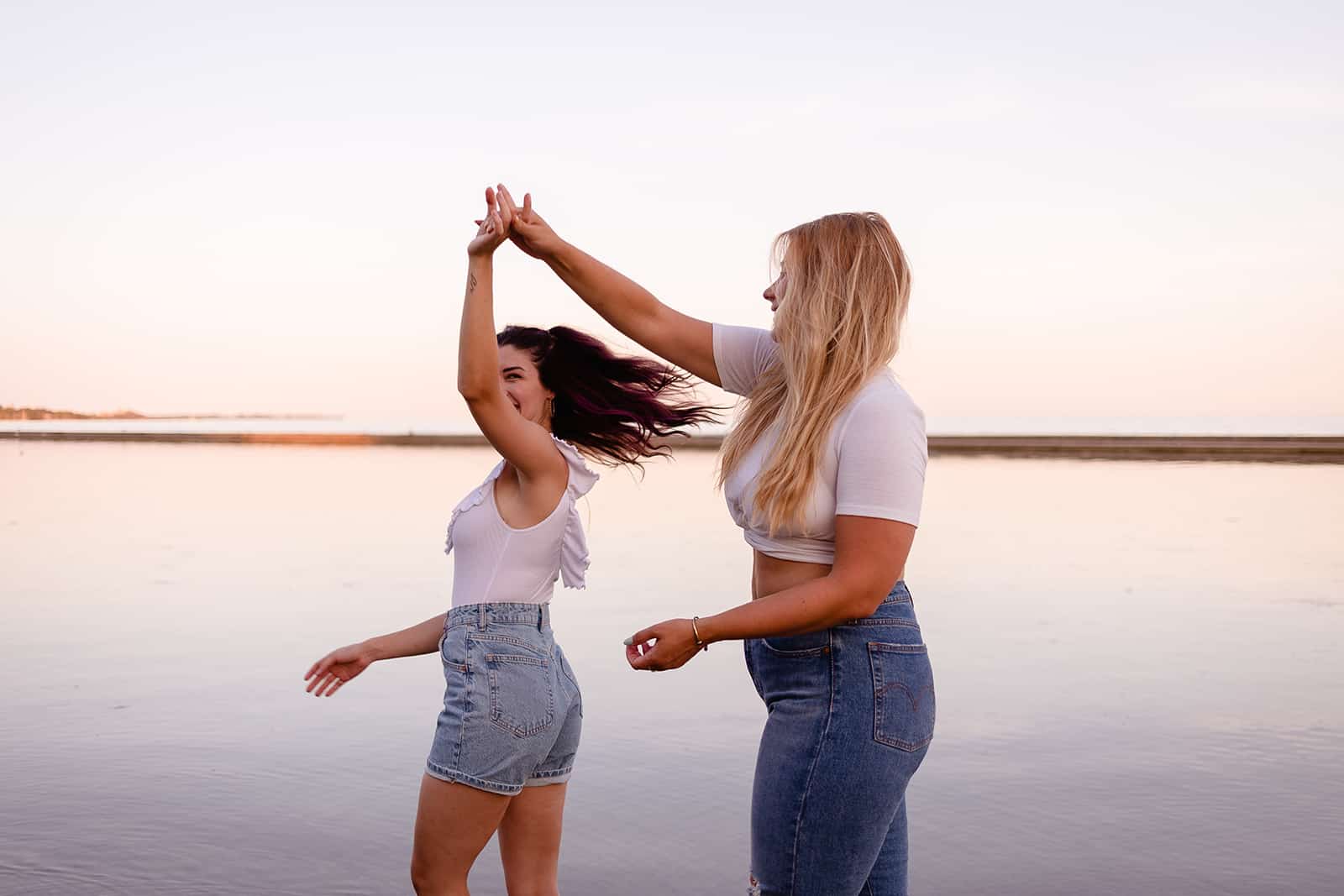 two happy female friends dancing on the beach during sunset