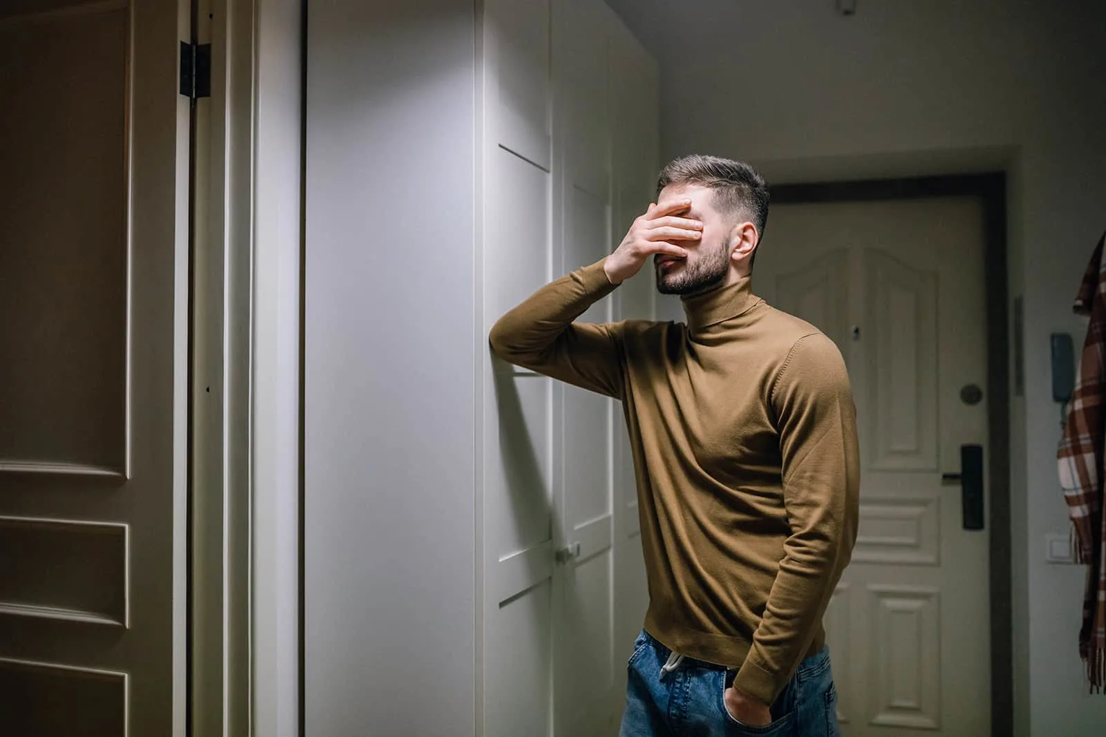 upset man covering face with palm and standing in apartment