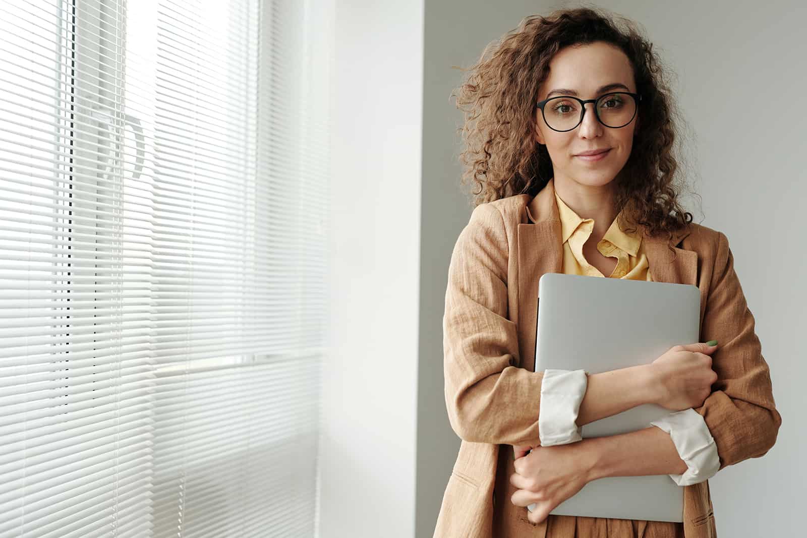 woman holding a laptop and standing near the window