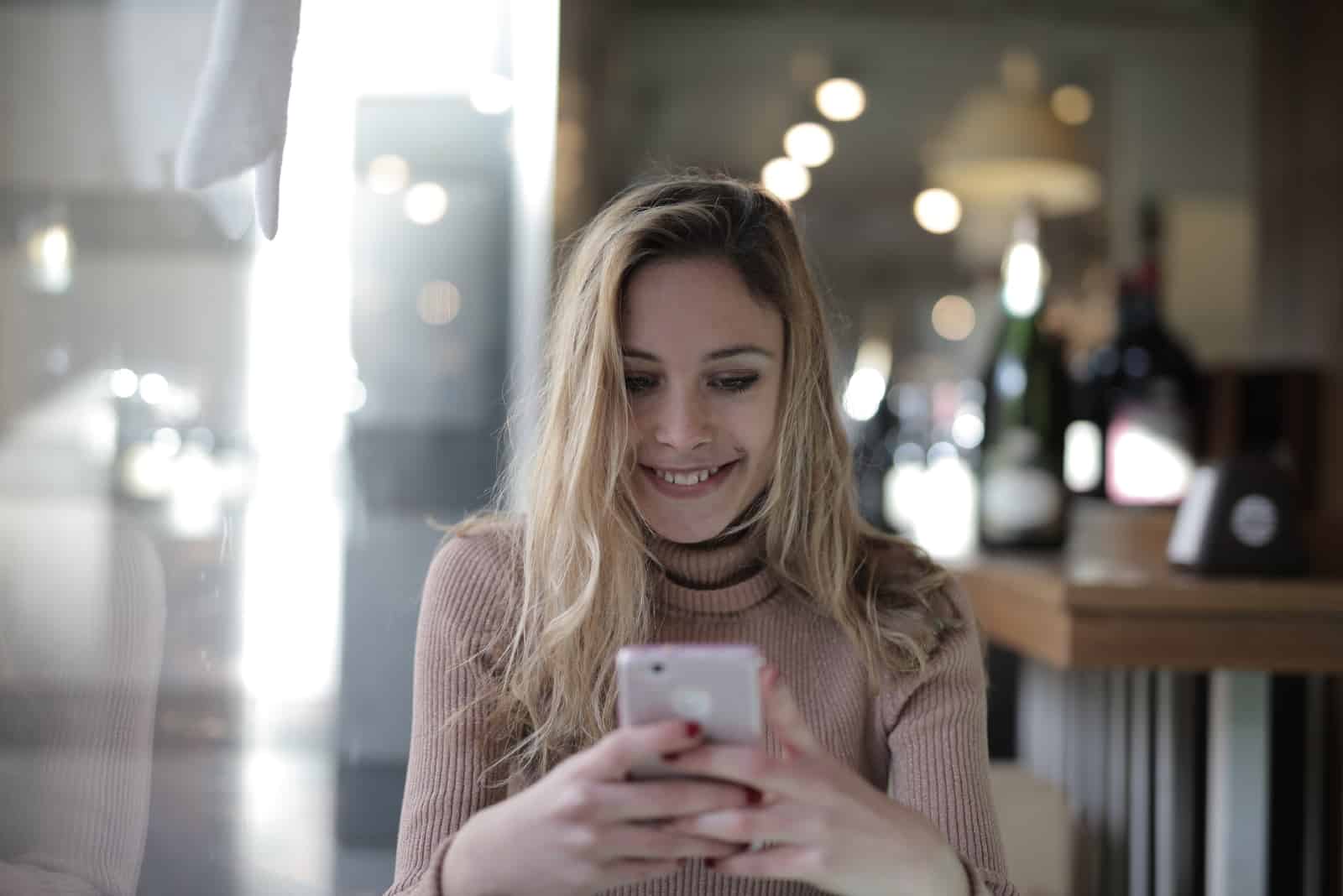 mulher feliz a segurar o telemóvel enquanto está sentada à mesa