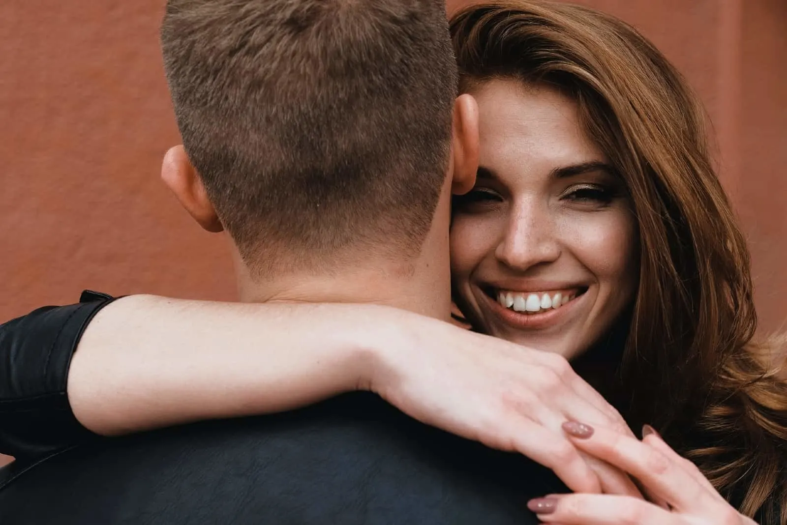 happy woman hugging man while standing near wall