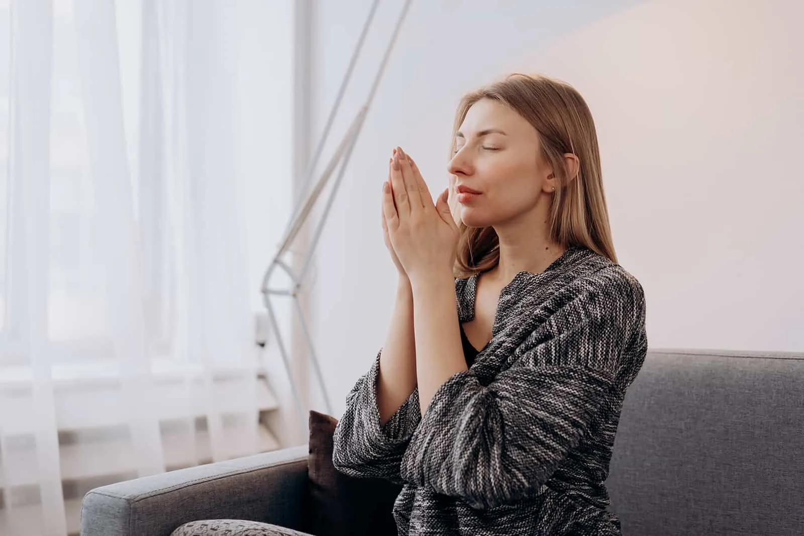  woman praying with eyes closed while sitting on couch