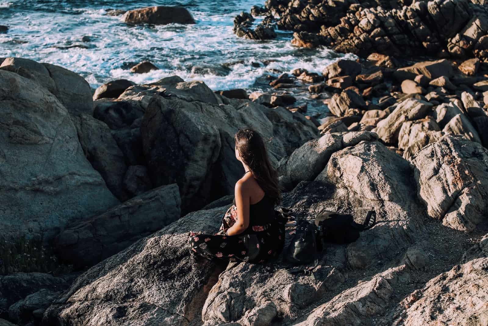 mujer sentada en una roca mirando al mar