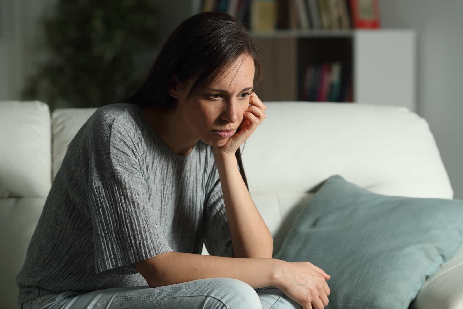 mujer triste con top gris sentada en un sofá