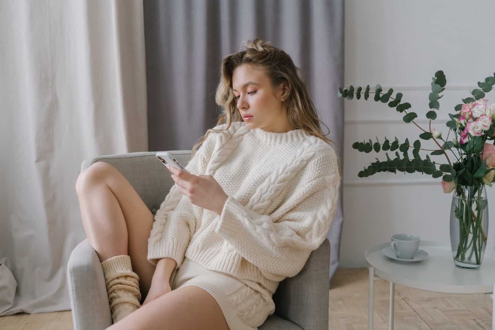 donna che usa lo smartphone seduta su una poltrona grigia