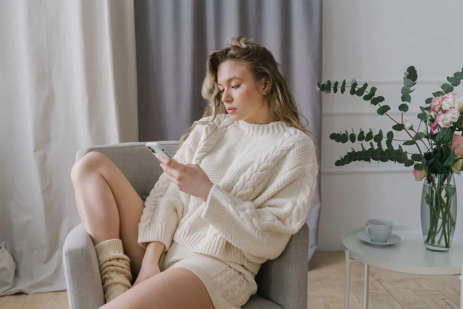 woman using smartphone while sitting on gray armchair