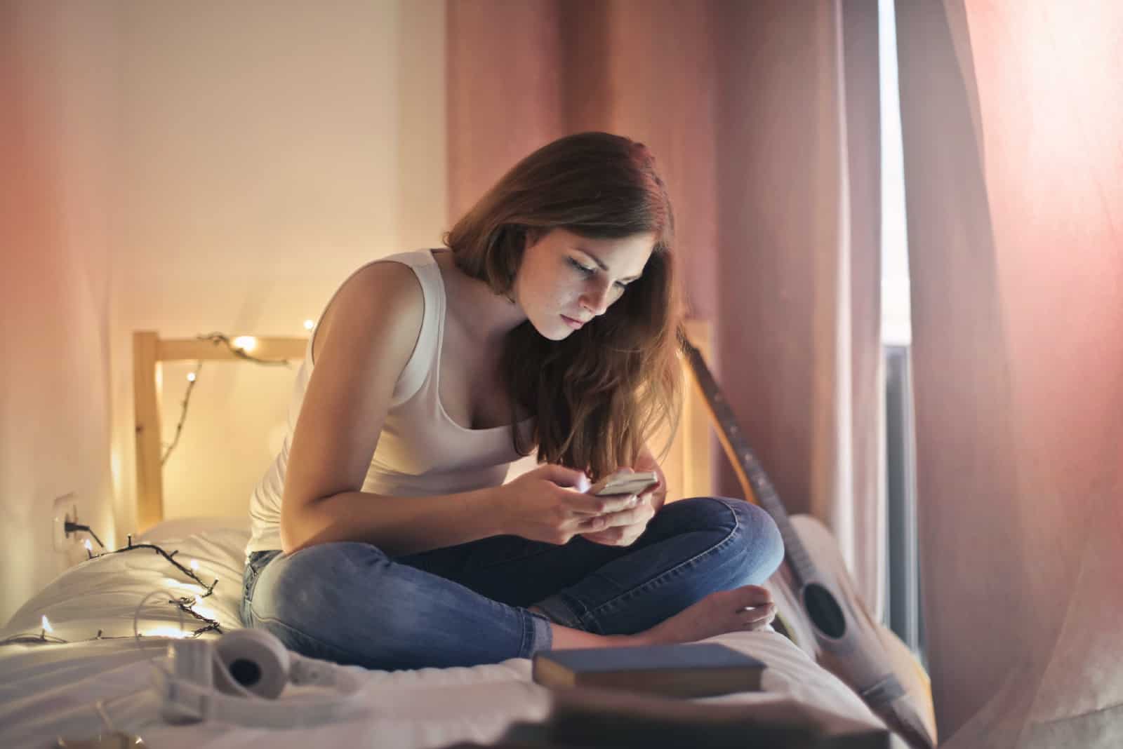 donna che usa lo smartphone seduta sul letto