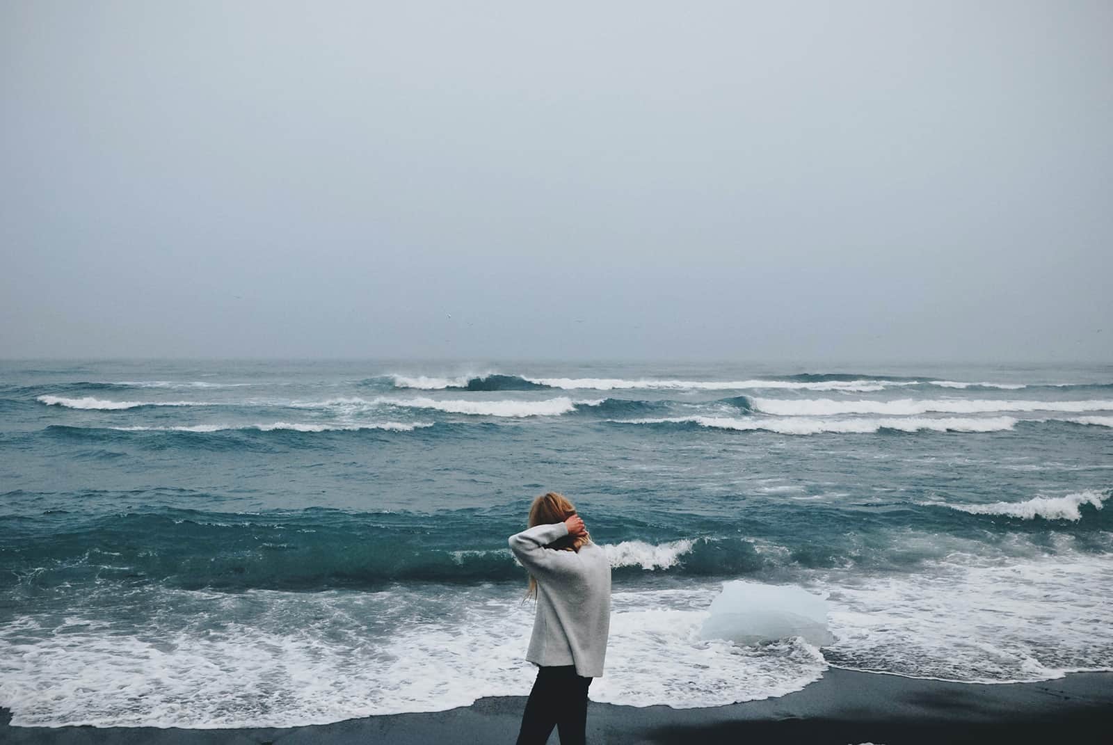 donna che cammina da sola sulla riva del mare e osserva le onde