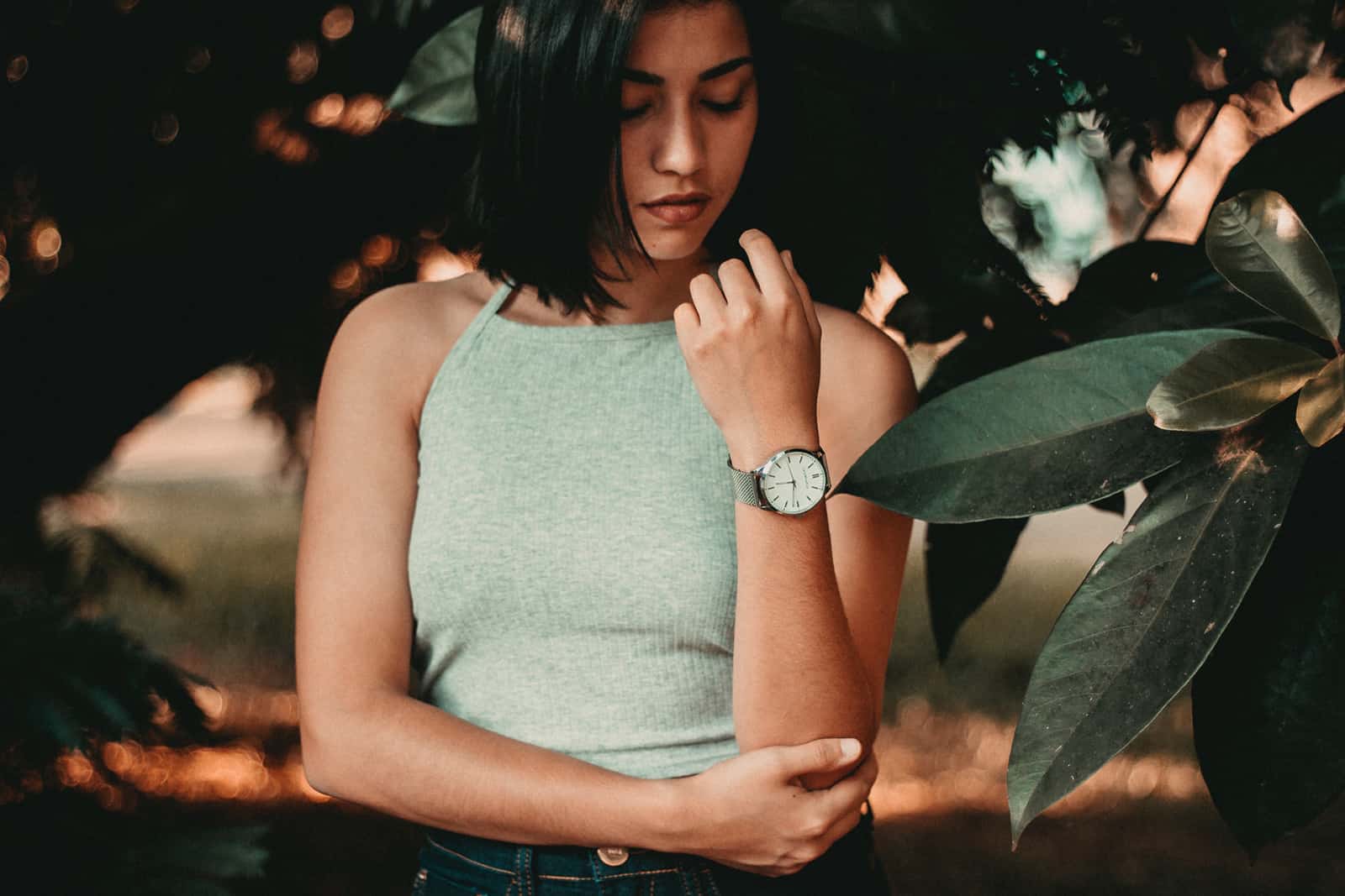woman wearing a wristwatch looking at it while standing near the plants