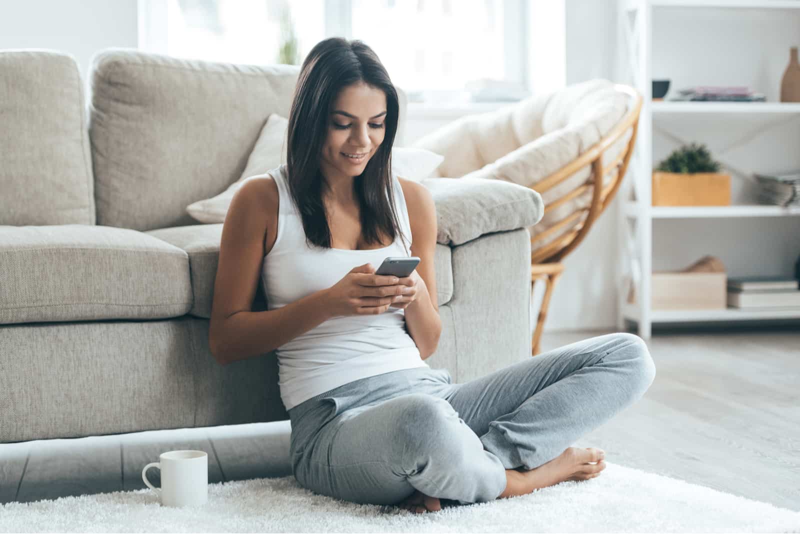 uma mulher sentada no chão a beber café e uma chave ao telefone