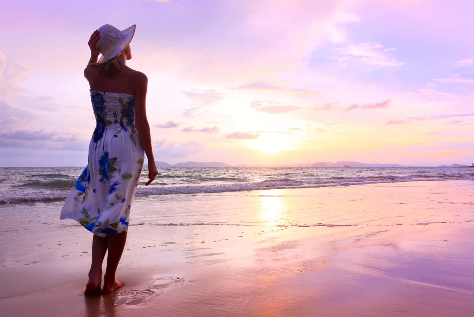 a woman with a hat on her head is standing on the beach