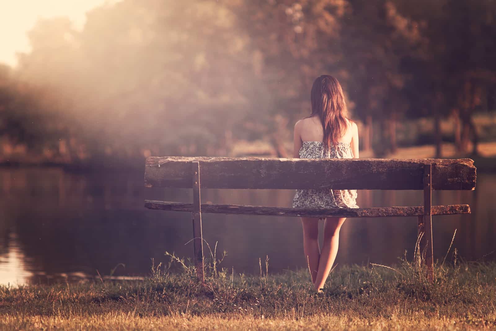 the woman sits on a bench and looks out at the lake