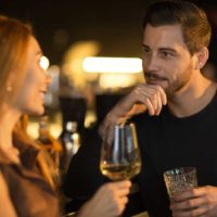 a man and a woman stand and talk over drinks