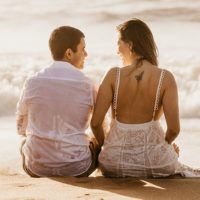 casal sentado na praia ao pôr do sol