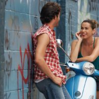 una donna sorridente siede su una moto e parla con un uomo