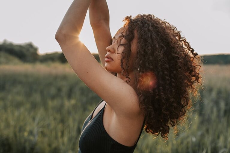 woman with eyes closed putting her arms up stands in the field