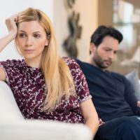 unhappy woman turning back from her husband sitting close to her on the couch