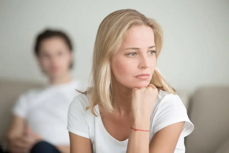 Serious sad woman thinking over a problem while husband sitting behind her