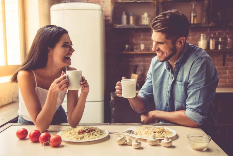 um homem e uma mulher sorridentes sentam-se à mesa e tomam o pequeno-almoço