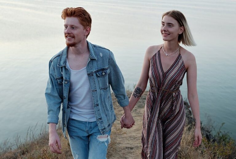 casal sorridente de mãos dadas num penhasco