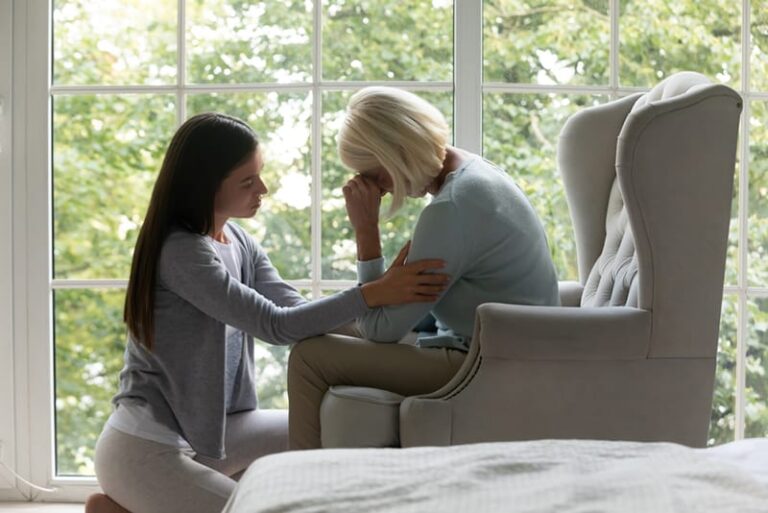 a daughter comforting her mother sitting in the armchair
