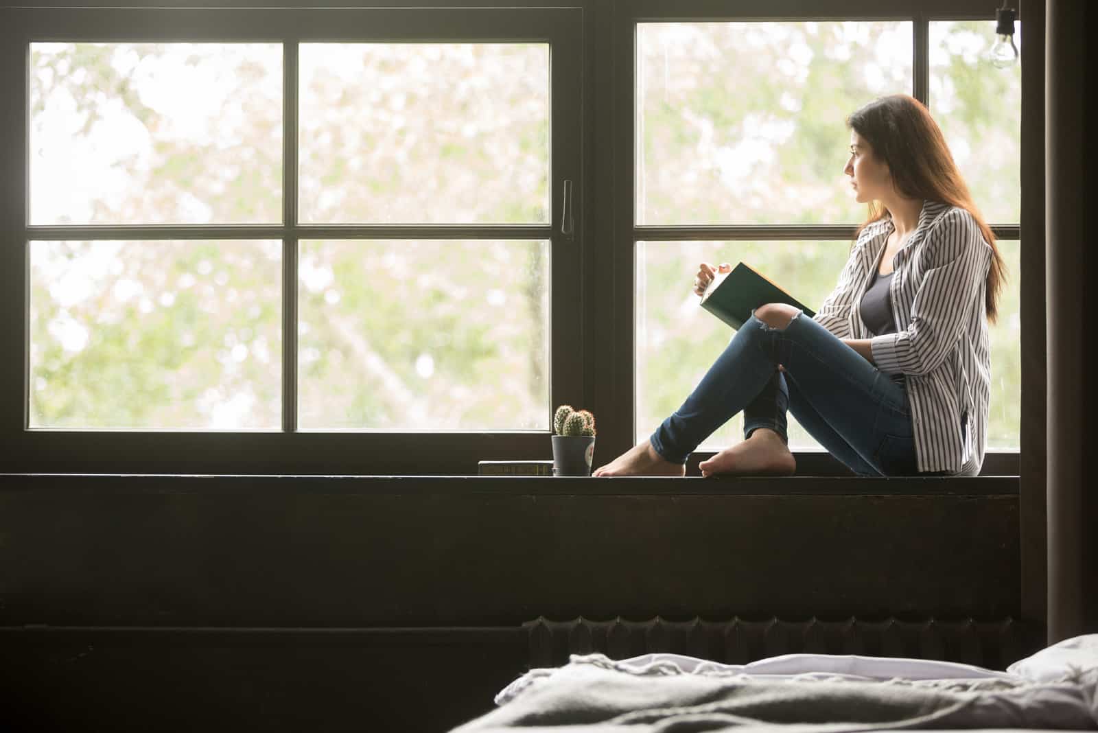 una bella donna seduta alla finestra che legge un libro