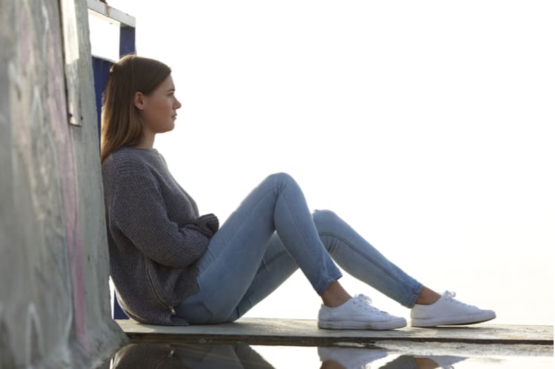 a brown-haired woman sits on a wooden mat and looks ahead