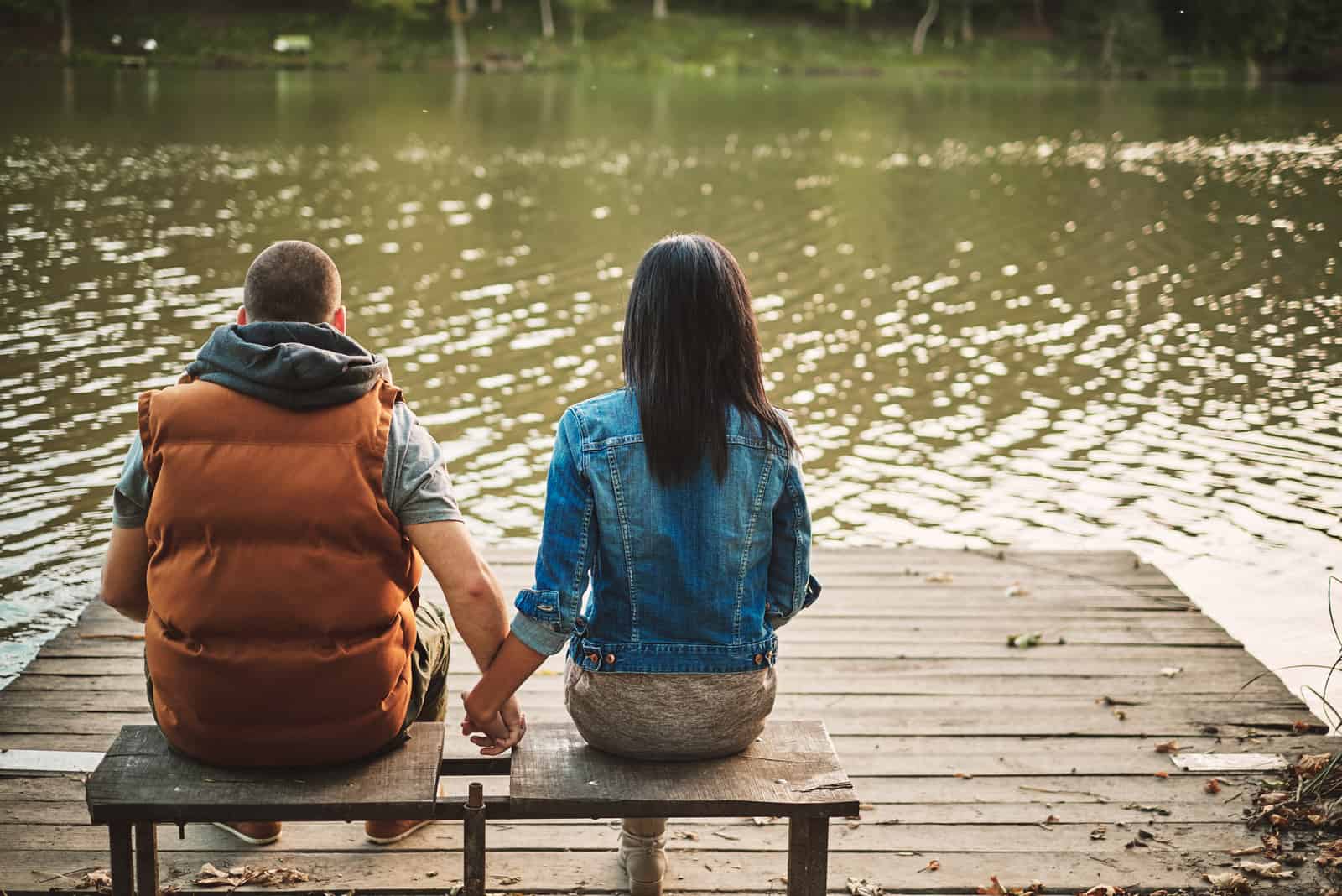 um casal apaixonado sentado num banco de mãos dadas e a olhar para o rio