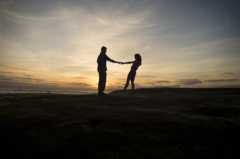 Una coppia di innamorati che si tiene per mano sulla spiaggia durante il tramonto