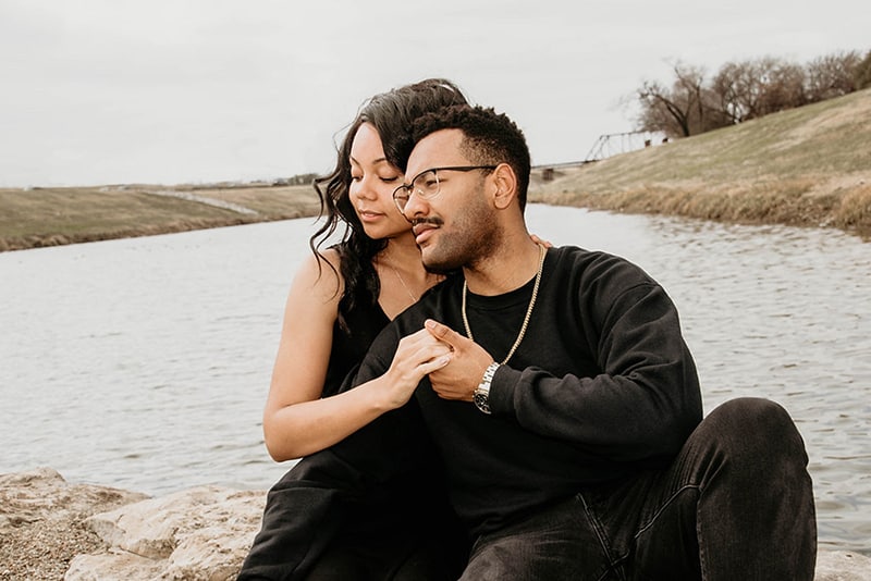 una pareja de enamorados cogidos de la mano sentados cerca del río