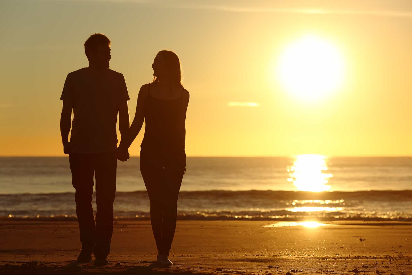 un uomo e una donna camminano lungo la spiaggia tenendosi per mano