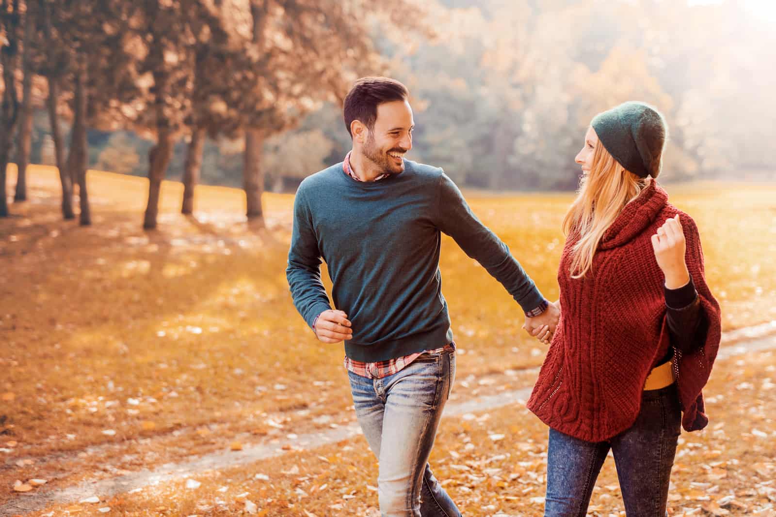 a man and a woman holding hands and running through the park