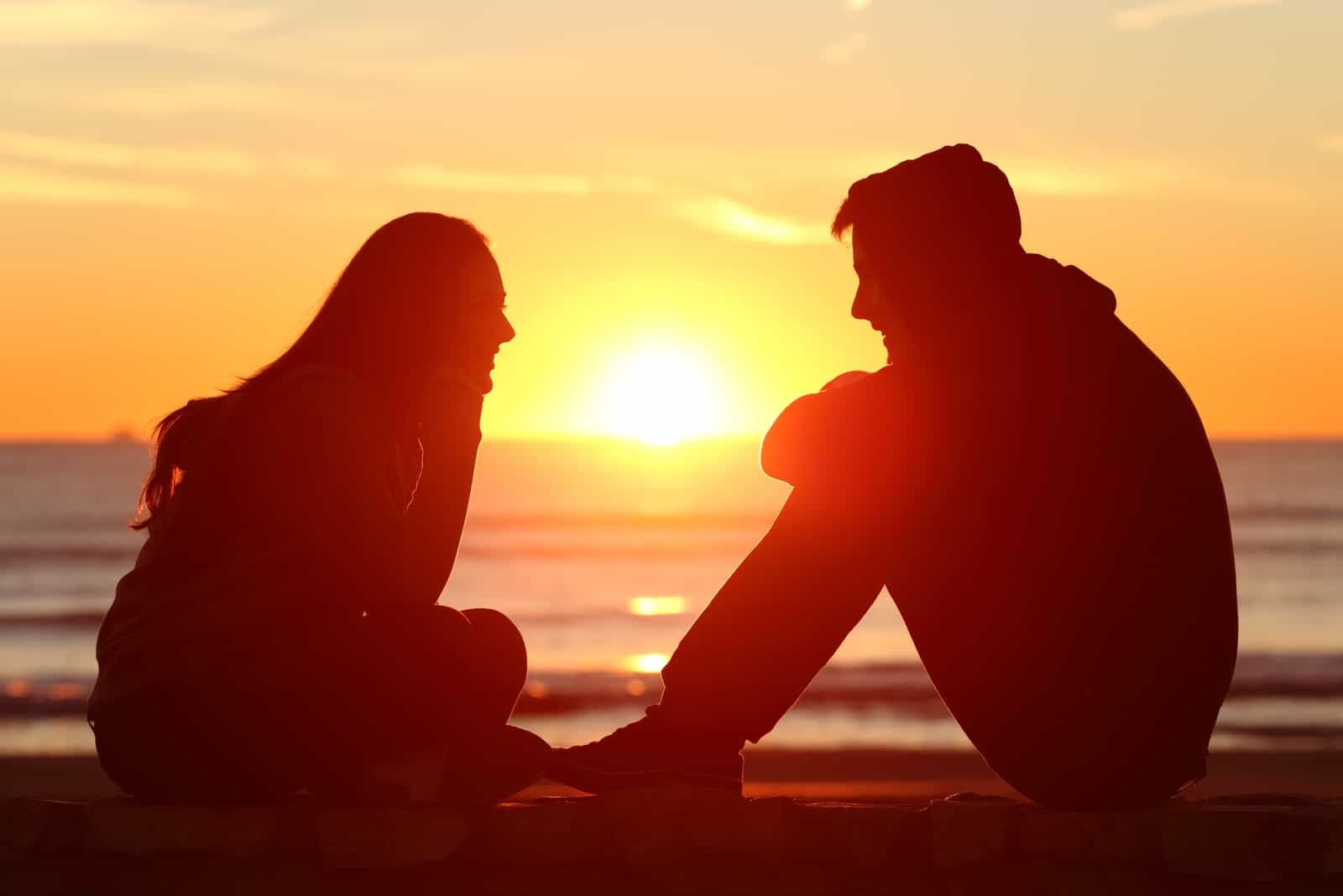 um homem e uma mulher sentam-se ao pôr do sol e conversam