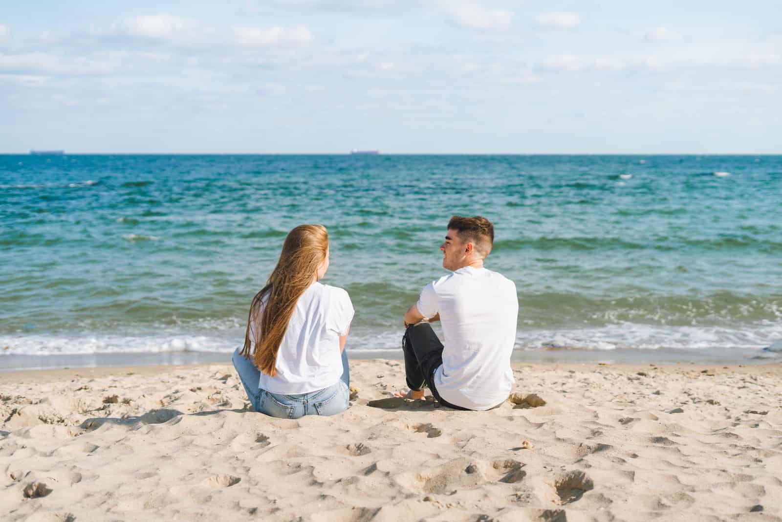 a man and a woman sit on the beach and talk