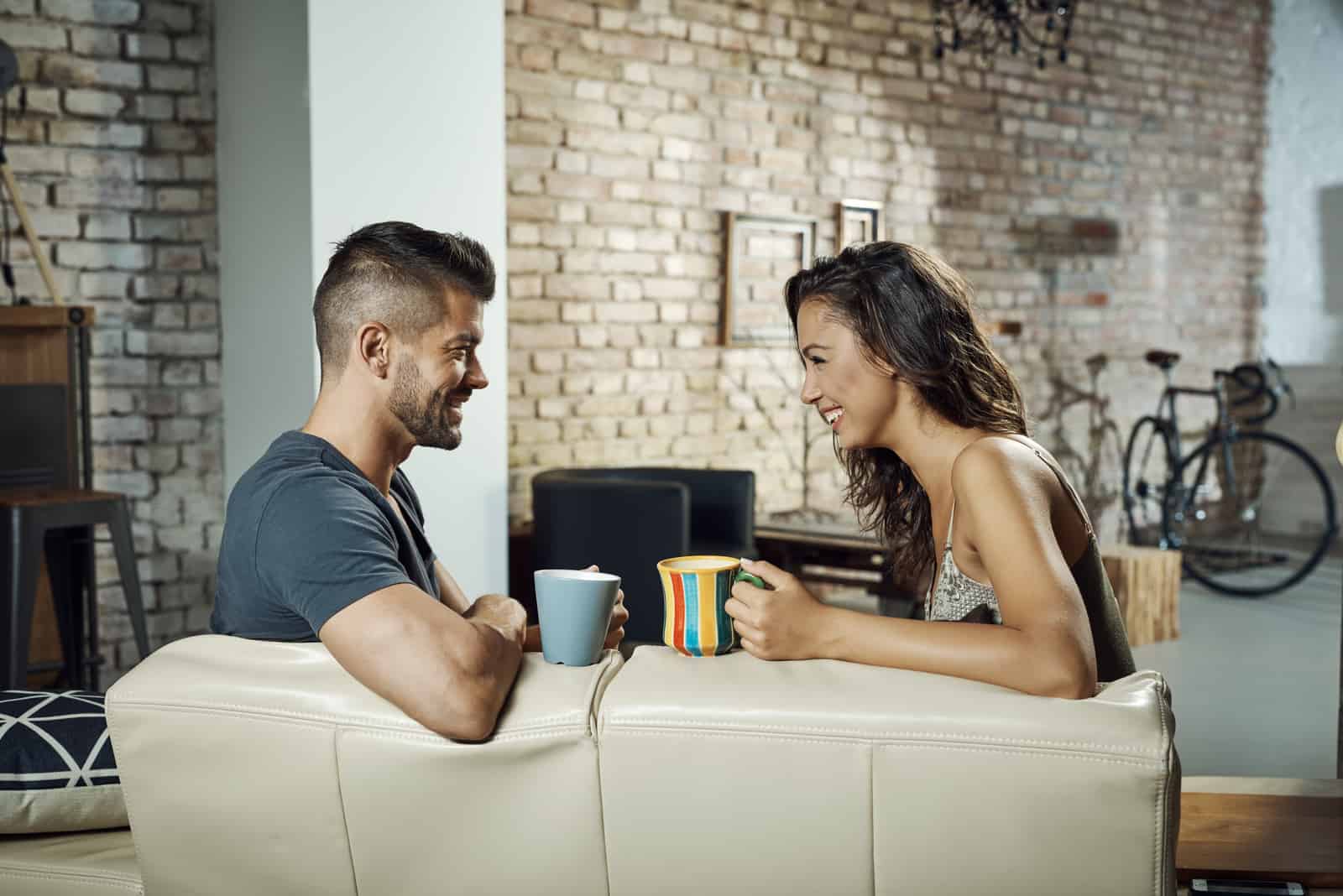 a man and a woman sit on the couch drinking coffee and talking