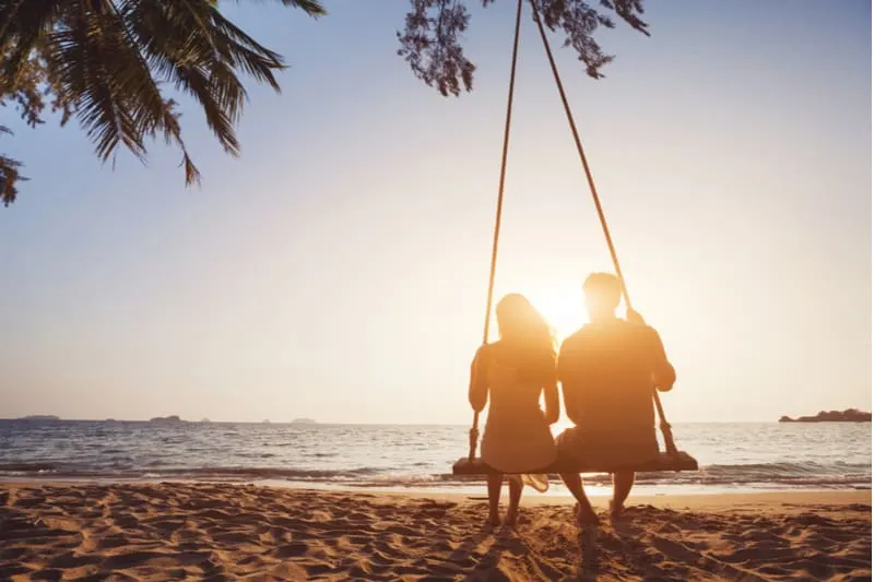 a man and a woman sitting on a swing on the beach